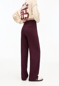 Bordeaux brede beenbroek met een hoge taille, zachte stof en twee achterzakken. Gepaard met een cropped beige trui met een bordeaux graphic.