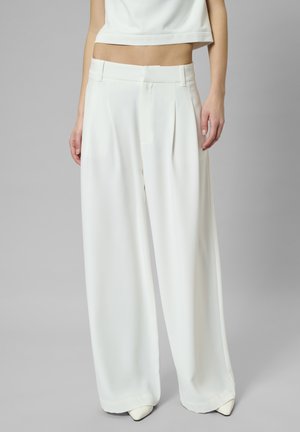 Weiße, weit geschnittene Hosen aus glattem Stoff, mit Falten, einem strukturierten Bund und einem fließenden Design. Kombiniert mit einem cropped Top.