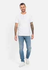 Hvid bomulds henley-shirt med tre træknapper, parret med lyseblå slidte jeans og hvide sneakers. Casual pasform og moderne design.