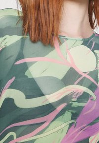 Gennemsigtig top i let stof med en grøn bund, der har abstrakte pink og mint mønstre, rund halsudskæring og struktureret overflade.