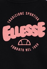 Svart stoff med en stor rosa Ellesse-logo, med rundede bokstaver. Teksten sirkler "Tradizione Sportiva" og "Fondato nel 1959" på toppen og bunnen.