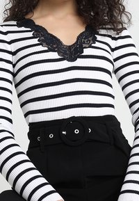 Haut côtelé à rayures noires et blanches avec un col en V en dentelle, associé à un pantalon noir taille haute avec une boucle de ceinture circulaire.