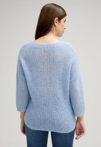 Jasnoniebieski sweter robiony na drutach o luźnym fasonie, z szerokim dekoltem, rękawami trzy czwarte oraz subtelnym detalem w postaci guzików z tyłu.