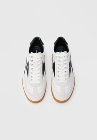 Białe i szare trampki z czarnymi akcentami, wykonane z mieszanki gładkich i zamszowych tekstur, z płaskimi sznurowadłami oraz gumową podeszwą.