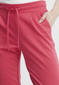 Pink joggers made of soft fabric, featuring a drawstring waistband, front pockets, and subtle side pleats for a tailored look.
