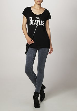 Sort t-shirt med hvid tekst "The Beatles", parret med grå skinny jeans og sorte ankelstøvler. Accessories inkluderer en sort skuldertaske.