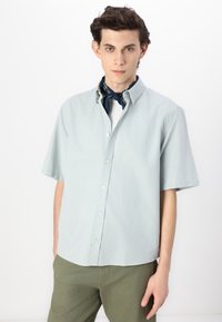Chemise à manches courtes vert clair à boutons, fabriquée en tissu doux, avec un col classique et une texture lisse, associée à un pantalon vert olive.