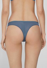 Blaue nahtlose Tanga-Unterwäsche mit glatter Textur und minimaler Bedeckung, ausgestattet mit einem tief sitzenden Bund und ohne sichtbare Beschläge.