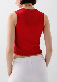 Punainen ribbineuleinen crop top, jossa on aaltoileva helma ja teksturoitu kangas; yhdistetty valkoisiin joustovyötäröisiin housuihin, joissa on yksinkertainen pyöreä pääntie.
