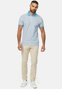 Polo t-shirt i lys blå med et rutenet mønster i rød og hvid, parret med beige bukser og hvide sneakers. Korte ærmer og kravedesign.