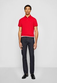 Red cotton polo shirt with short sleeves, dark denim jeans, and black loafers. Simple design, fitted shape, small logo on the shirt.