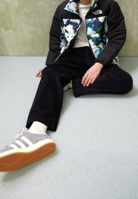 Chaqueta tipo puffer con un patrón floral en tonos de azul, pantalones de pana negros y zapatillas grises con rayas blancas y suela de goma.