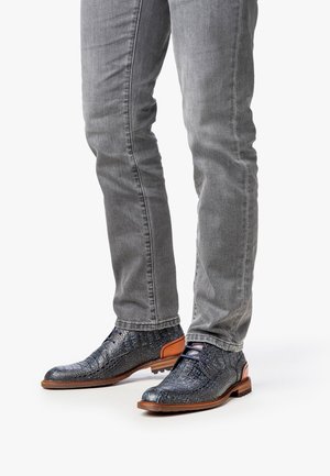 Zapatos de cuero con patrón de cocodrilo azul y acentos marrones, combinados con jeans ajustados grises, que exhiben una textura detallada y un diseño elegante.