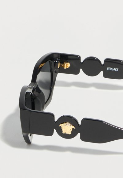 Μαύρα γυαλιά ηλίου Versace με παχιές πλευρές που φιλοξενούν ένα χρυσό έμβλημα Medusa και το όνομα της μάρκας στο εσωτερικό του βραχίονα.