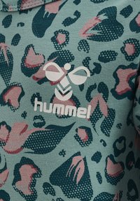 Grön tyg med ett färgglatt leopardmönster i rosa och marinblått. Framträdande vit "hummel"-logga och en bi-grafik. Mjukt, strukturerat material.