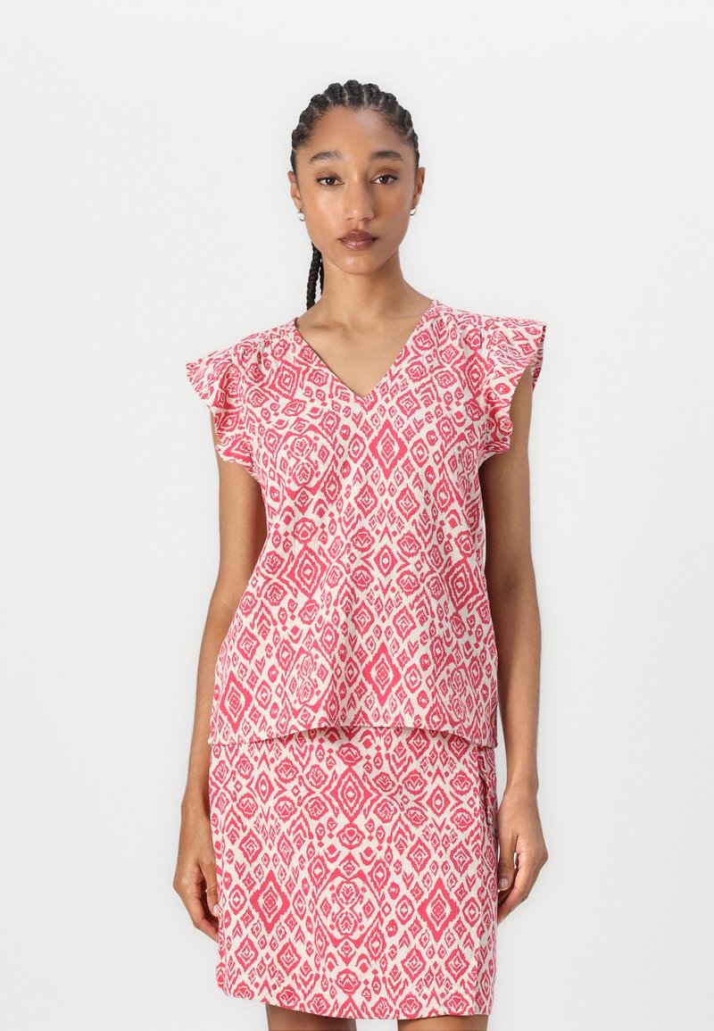 Rosa gemusterte Bluse mit V-Ausschnitt und Schmetterlingsärmeln, kombiniert mit einem passenden Rock. Der Stoff weist geometrische Designs in Weiß auf.