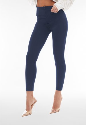 Leggings a vita alta blu navy con una zip anteriore, realizzati in un materiale liscio ed elastico. Abbinati a scarpe con tacchi alti trasparenti.