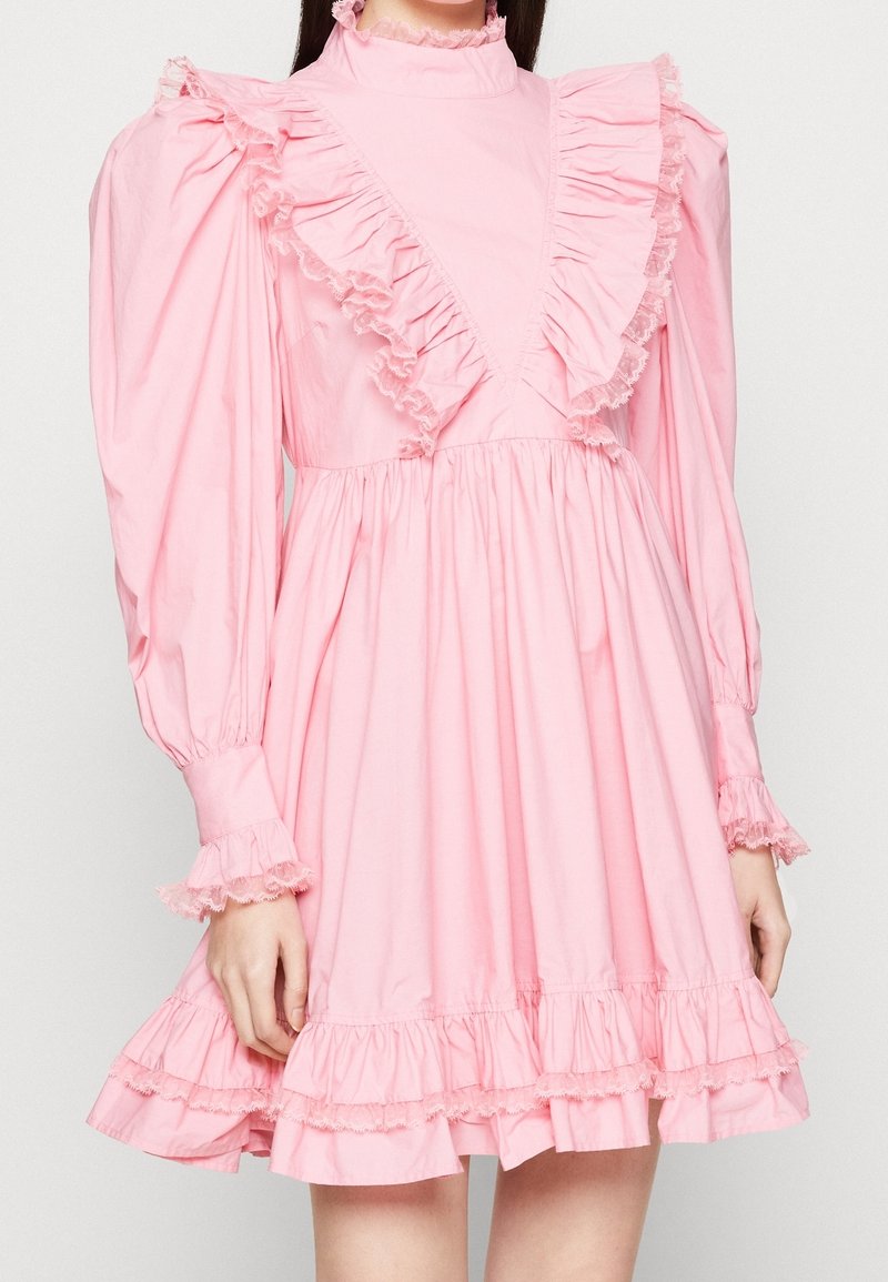 Robe rose à manches longues avec volants sur la poitrine, les poignets et l'ourlet, dotée d'épaules bouffantes et d'un col montant orné de dentelle.