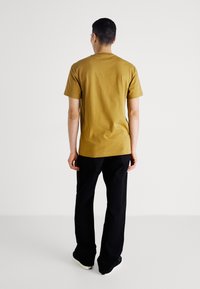 T-shirt a maniche corte di colore giallo senape con scollatura rotonda, abbinato a pantaloni neri. Design semplice, materiale in cotone, vestibilità comoda.