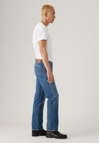 Blauwe spijkerbroek met een recht gesneden pijp, voorzien van een leren label aan de achterkant en een lichte wassing. Gepaard met een slim fit wit t-shirt en zwarte laarzen.
