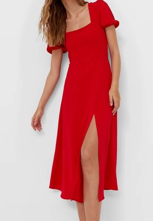 Rode jurk met een vierkante halslijn, korte pofmouwen en een hoge split tot boven de dij, gemaakt van een gladde stof met een vloeiende silhouet.