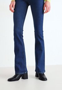 Uppblåsta mörkblå denimjeans med en mjuk textur. Matchas med svarta klackboots som har kvadratisk tå och kraftig klack.