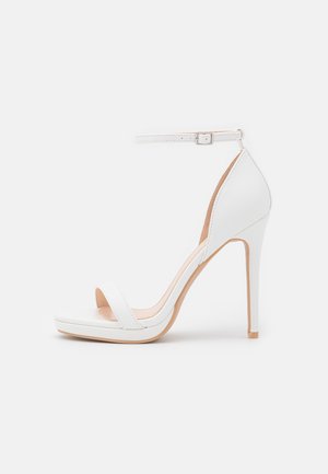 Sandalia de tacón alto blanca con punta abierta, tira en el tobillo y plataforma. Fabricada en material sintético suave, con un tacón esbelto y un diseño minimalista.