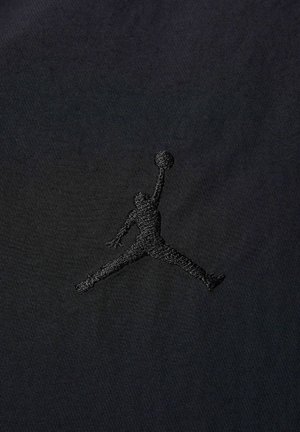 Sort stof med et præget sort Jumpman-logo, der viser et tekstureret design mod en glat baggrund.