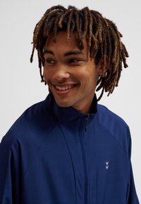 Navyblauwe zip-up jack met een hoge kraag, voorzien van schuine naden en een klein logo. Zachte textuur en lichtgewicht materiaal.