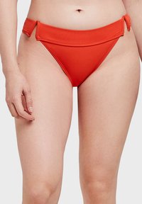 Červené bikiny s vysokým pasem, vyrobené z hladkého materiálu. Obsahují detail se šněrováním na boku a minimalistický design.