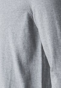 Grauer, weicher Strickpulloverstoff mit sichtbarer Textur, ausgestattet mit einem Rundhalsausschnitt und leicht taillierten Ärmeln. Nahtdetail an der Seite.