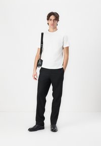 Bílý krátký rukávový tričko spárované s černými přizpůsobenými kalhotami a černými koženými botami. Malá černá crossbody taška visí z popruhu.