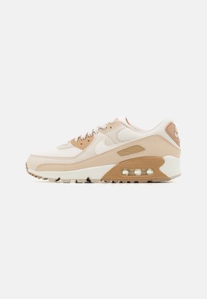 Beżowo-białe trampki Nike Air Max z widoczną poduszką powietrzną, białym logo Swoosh i teksturowaną podeszwą na jednolitym tle.
