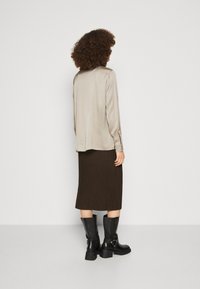 Beige Satinbluse mit langen Ärmeln, kombiniert mit einem braunen, gerippten Midirock und schwarzen kniehohen Stiefeln, von hinten betrachtet.