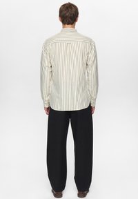 Gestreept overhemd met knopen in crème en marineblauw, met een rugpas en manchetten. Gecombineerd met loszittende zwarte broek en bruine schoenen.