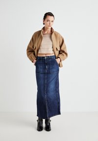 Brown oversized bomber jacket, striped cropped sweater, denim maxi skirt, black ankle boots with buckles. Clean, casual style.