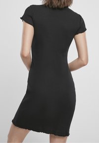 Schwarzes, geripptes Kleid mit kurzen Ärmeln, taillierter Silhouette und fransigen Saumdetails. Weicher Stoff und mittlere Oberschenkellänge.