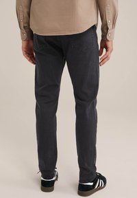 Tmavě šedé slim fit džíny vyrobené z denimu s hladkou strukturou, s kapsami vzadu, doplněné zeleno-bílými teniskami.