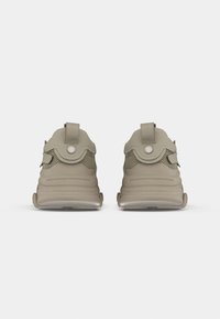 Beige Sneakers mit einem strukturierten Mesh-Obermaterial und glatten Gummisohlen. Sie verfügen über eine Schlaufe an der Ferse und kreisförmige Metallakzente.