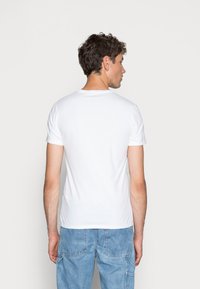 Hvid bomulds T-shirt med korte ærmer, rund halsudskæring og en glat tekstur, set fra ryggen.
