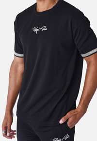 La camiseta negra de canalé presenta bordado "Project x Paris" en el pecho, con puños acentuados en plateado. La tela es texturizada y ajustada.