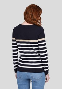 Pull bleu marine et blanc rayé avec une bande horizontale dorée à l'épaule ; il possède de longues manches et un col rond.