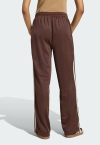 Pantalones de pista de satén marrón con un corte relajado, que cuentan con rayas laterales blancas y una cintura elástica, textura suave y sin marcas visibles.