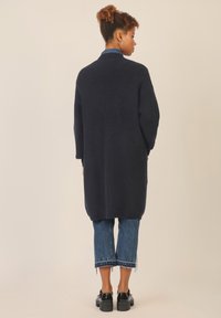 Granatowy długi kardigan, żebrowana tekstura, otwarty przód, boczne rozcięcia, w połączeniu z krótkimi dżinsami i czarnymi platformami.