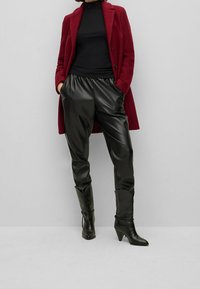 Bordeaux wollen jas over een zwarte coltrui, gecombineerd met zwarte leren broeken en puntige enkellaarsjes met een slank, taps ontwerp.