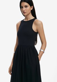 Vestido negro sin mangas con un busto ajustado y una falda acampanada. Fabricado con un tejido suave de textura lisa. Incluye bolsillos laterales y un diseño sencillo.