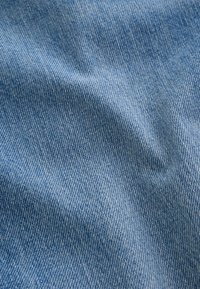 Gros plan sur un tissu denim bleu clair montrant un tissage sergé diagonal et de légers plis dans le matériau.