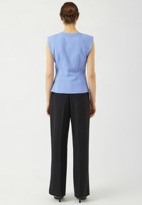 Ljusblå ärmlös topp med axelvaddar, figursydd design och diskreta sömmar, tillsammans med högmidjade svarta vida byxor.