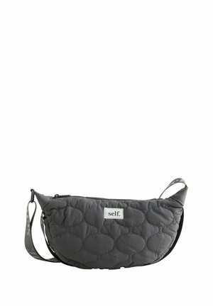 Sac bandoulière matelassé gris foncé en forme de croissant avec sangle réglable et étiquette blanche portant la mention «self.» au centre devant.