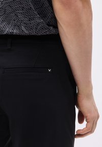 Δεξί χέρι ενός ατόμου που ακουμπάει δίπλα σε μαύρο παντελόνι με πίσω τσέπη και σε γκρι πουκάμισο με εξαγωνικό σχέδιο, που είναι τυλιγμένο μέσα.